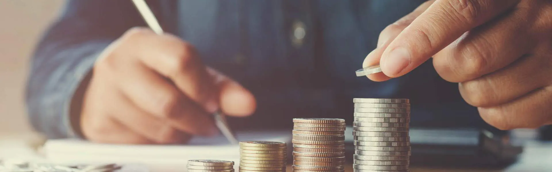 Hand holding pen and stacking coins