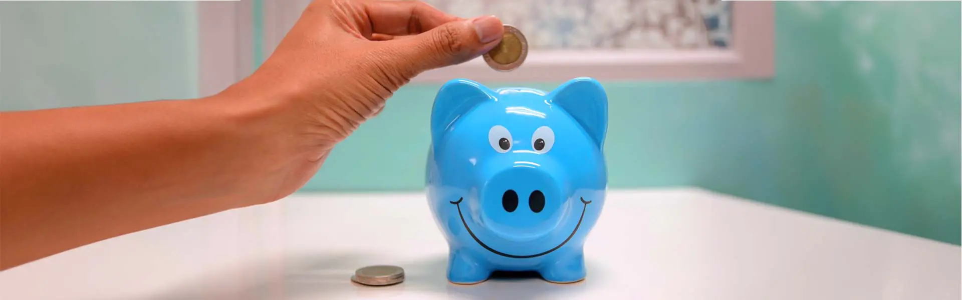 Hand putting coin into blue piggy bank